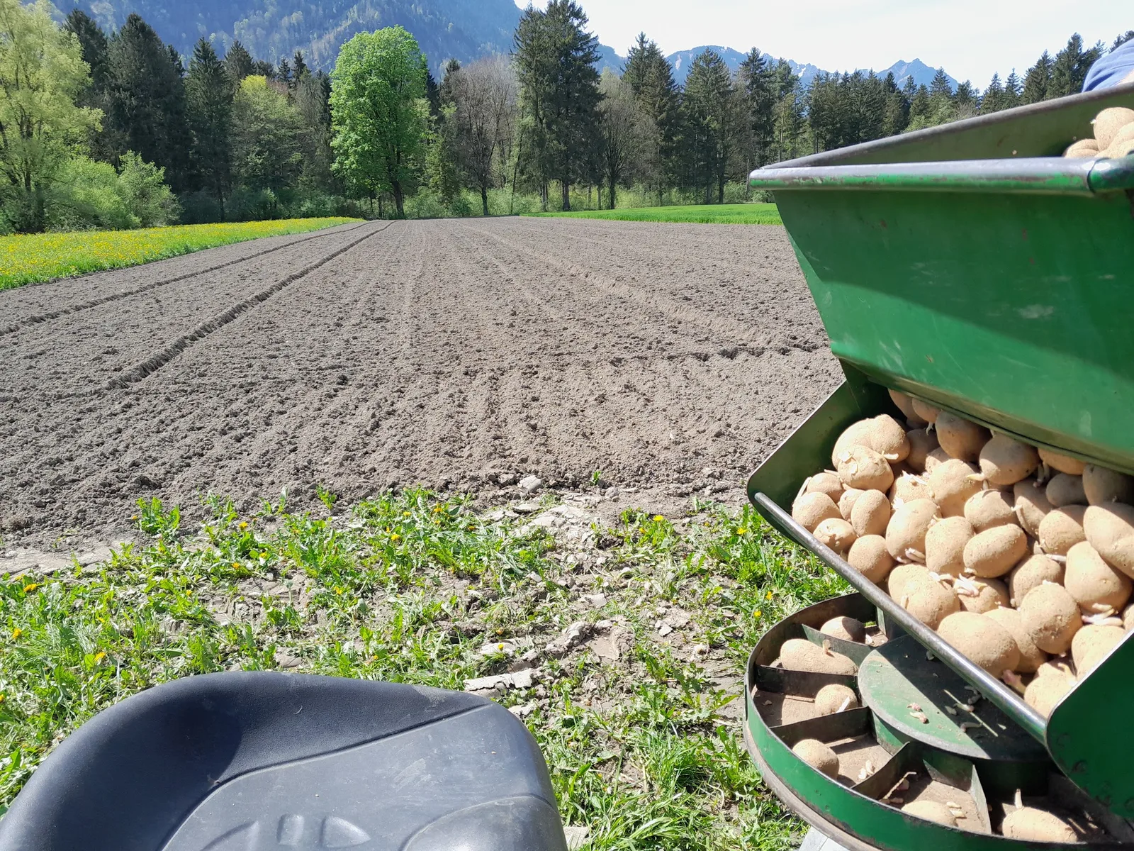 Kartoffelsetzmaschine am gepflügten Feld vor den Bergen